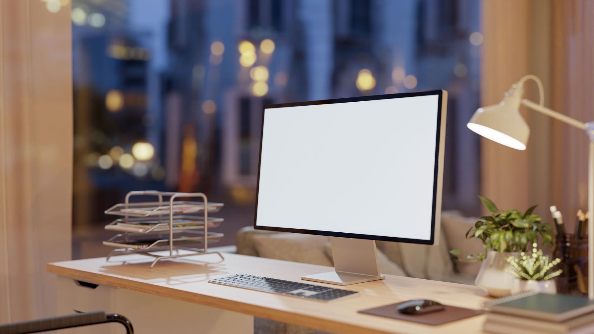 Un ordenador colocado sobre una mesa de madera en un salón moderno, iluminado por una cálida iluminación ambiental.